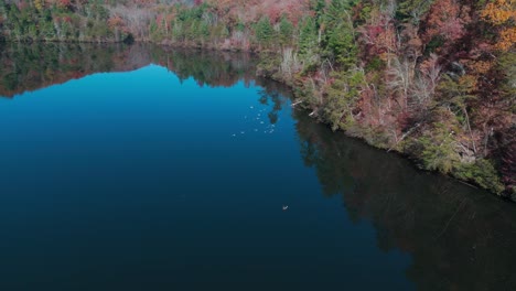 a lake mirroring its surroundings, encircled by the vibrant foliage of autumnal mountains - aerial panning