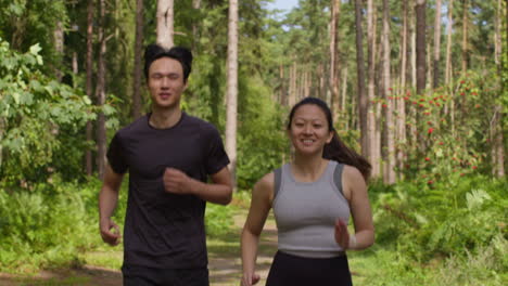 mid adult couple exercising doing work out outdoors running along track through forest towards camera wearing sports clothing 4