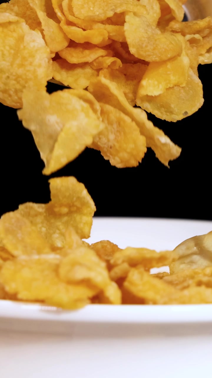 Uma colher levanta flocos de milho de uma tigela branca contra um fundo preto, destacando a textura e a cor do cereal.