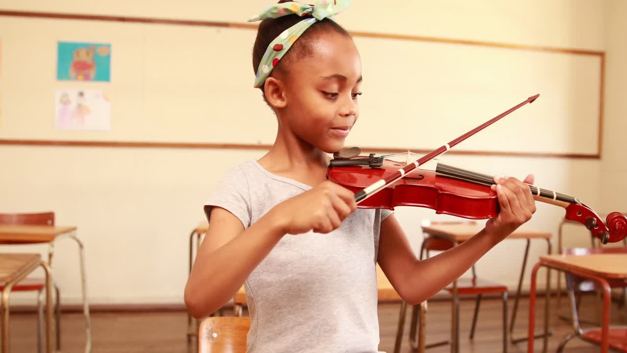 Cute pupil playing violin in classroom