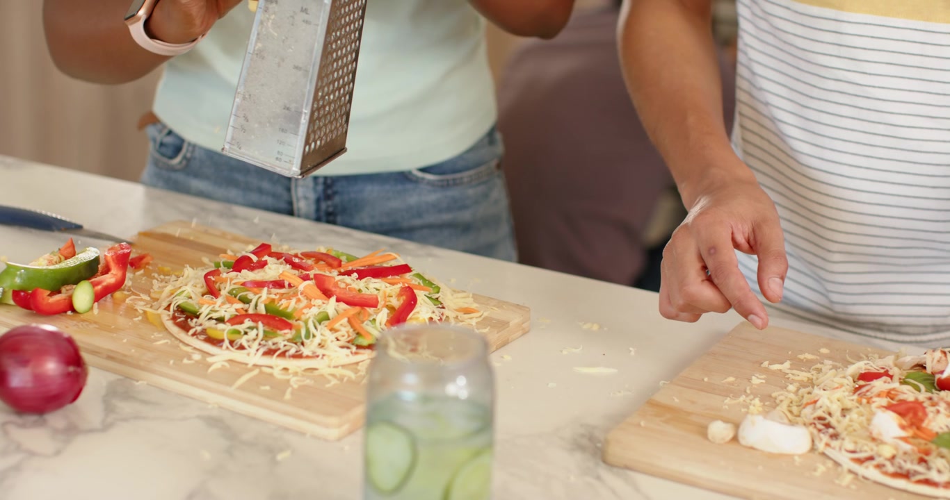 Amici africani che preparano pizze sul bancone, spostando i pomodori con un coltello e usando una grattugia.