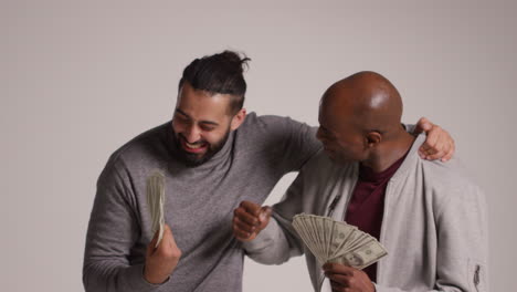 studio shot of two excited male friends celebrating winning cash prize throwing handful of 100 dollar bills in the air 1