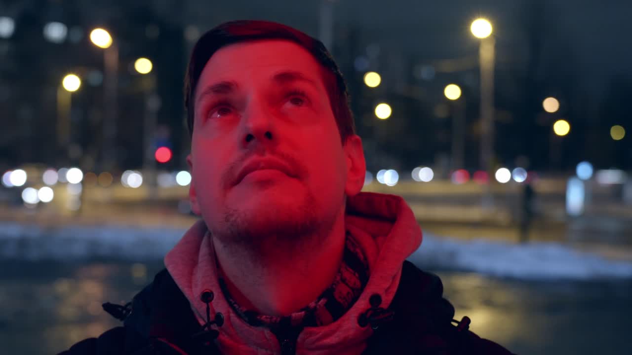 Calm caucasian man with short hair look up in red neon lights, street scene
