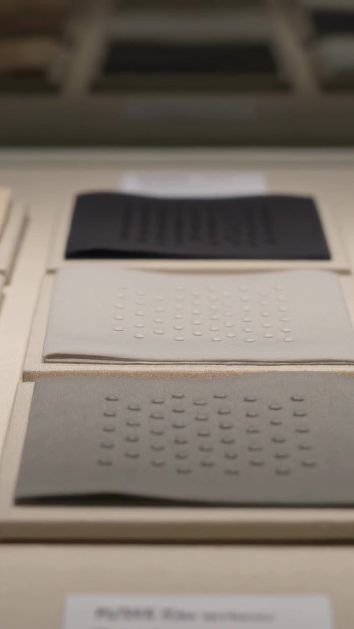 Video verticale: Telecamera che si inclina scansionando tre pannelli tattili in un espositore da galleria, rivelando le texture.