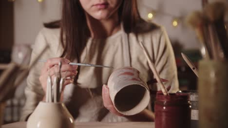 young woman potter coloring ceramic product with a brush then looks in the camera