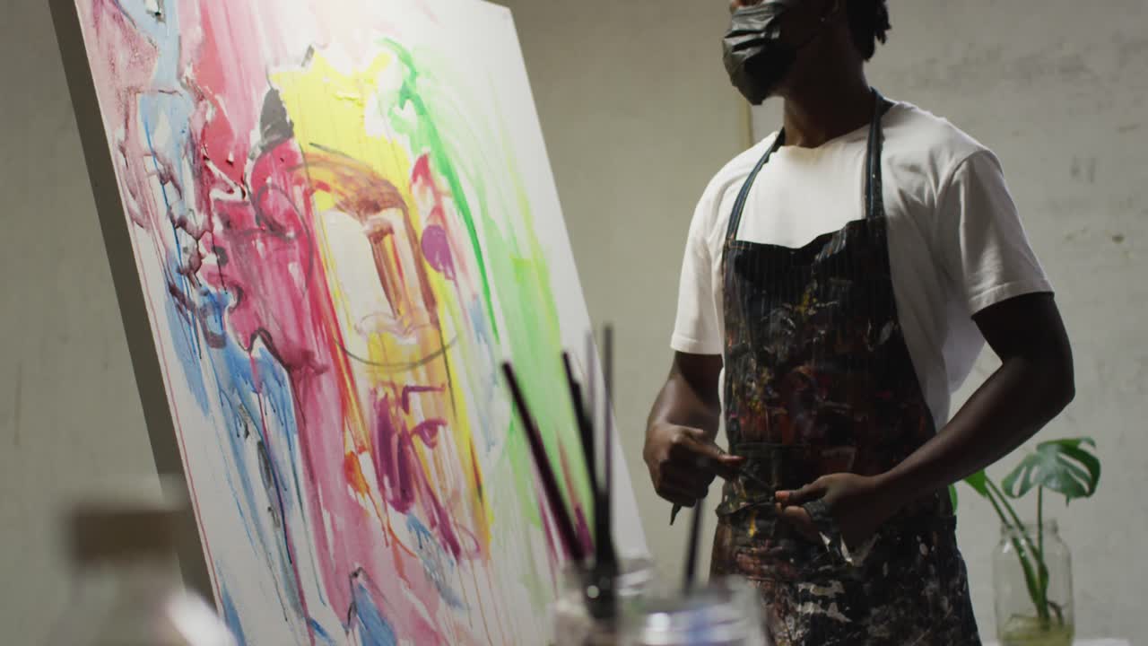 African american male artist wearing face mask tying his apron at art studio
