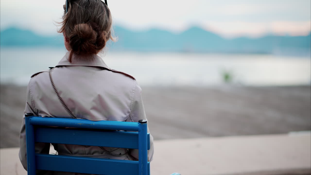 Woman in a trench coat sitting on a chair at the beach in France