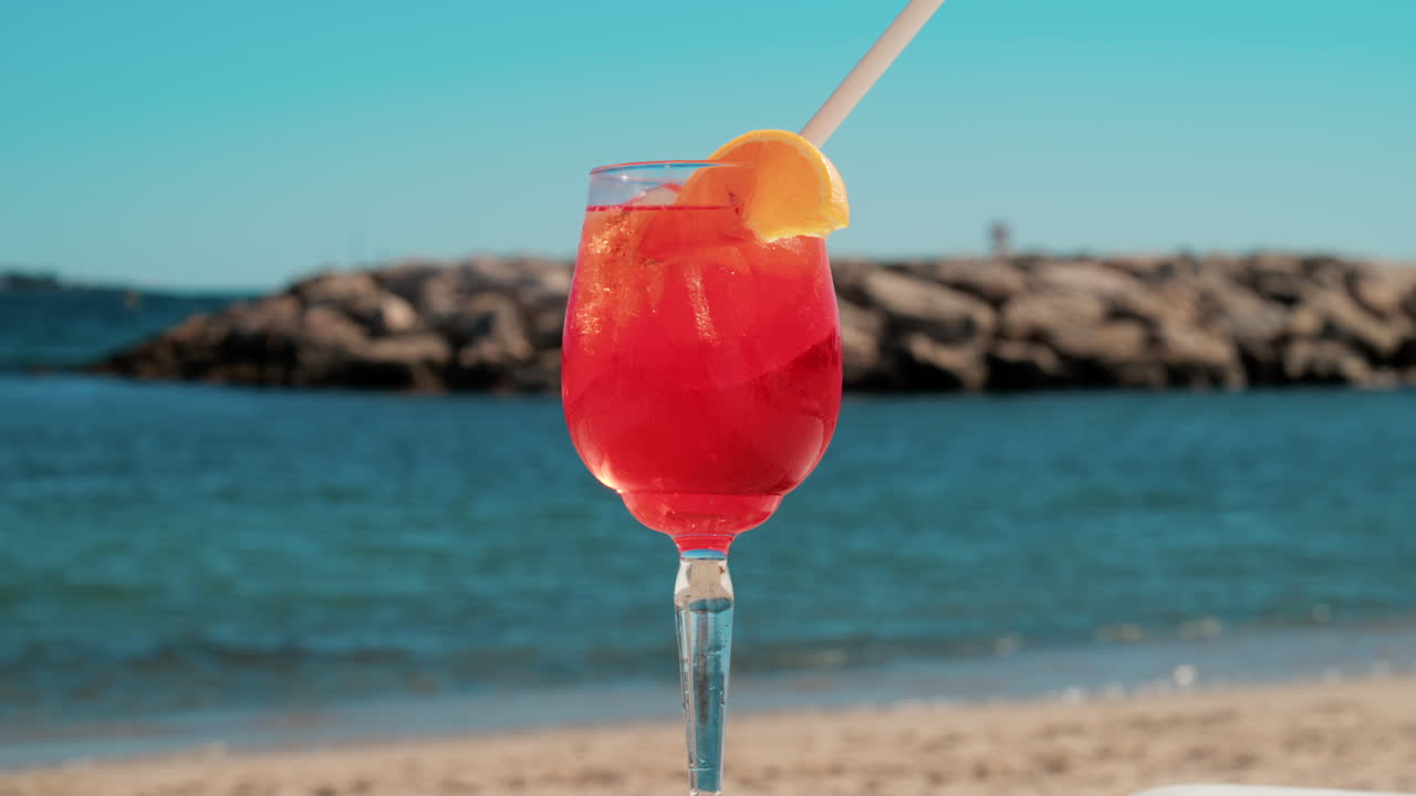 Un cocktail rinfrescante rosso-arancio con ghiaccio e fetta d'arancia sullo sfondo del blu intenso del Mar Mediterraneo