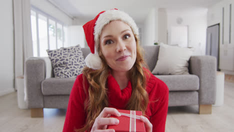 Mujer-Sorprendida-Con-Sombrero-De-Papá-Noel-Abriendo-Una-Caja-De-Regalo-Mientras-Realiza-Una-Videollamada-En-Una-Computadora-Portátil-En-Casa