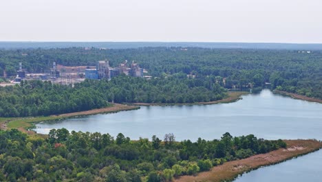 Moving-slowly,-panning-to-the-left-and-down-above-a-small-peninsula-and-a-large-lake-inlet-that-has-a-power-plant-behind-it