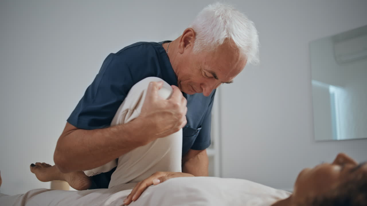 재활 클리닉에서 피지오테라피스트가 환자의 다리를 움직입니다.