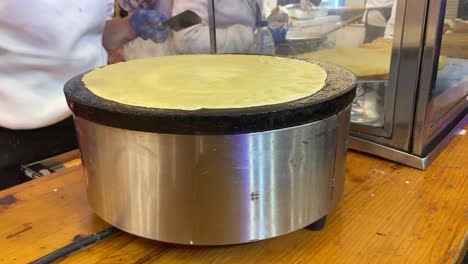 primer plano estático de la persona que da vuelta a una masa de crepes que se cocina en una fuente de calor redonda