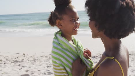 sonriente madre afroamericana toallando a su hija en una playa soleada