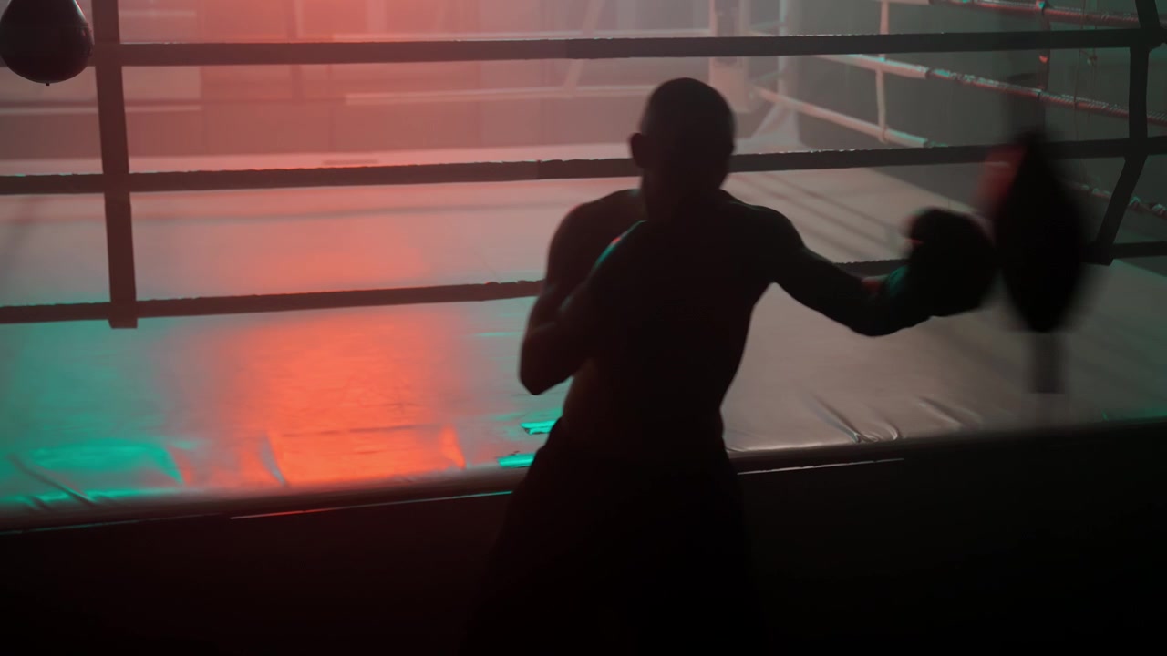 Pugile che si allena con il sacco veloce in un ring da boxe buio