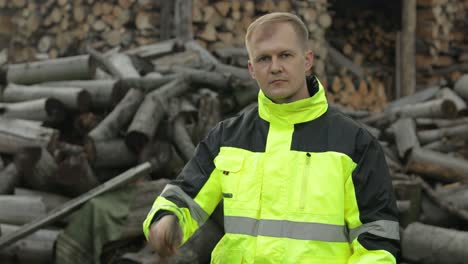 lumberjack in reflective jacket. man woodcutter hold small axe. sawn logs, firewood background