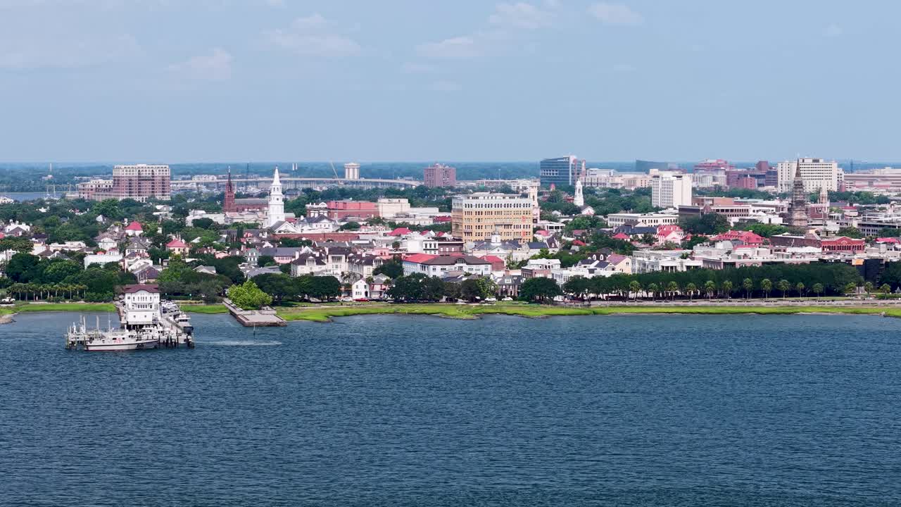 Drone footage shows the Charleston South Carolina skyline across the Cooper River harbor. The aerial view captures the waterfront, church steeples, historic downtown architecture and calm blue water