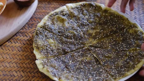 close up of a hand cutting zaatar manakish - flatbread topped with zaatar and olive oil. traditional arab food.