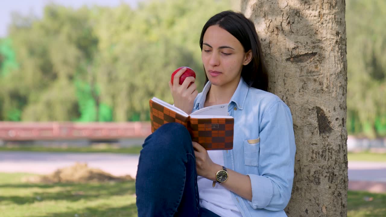 chica india comiendo manzana mientras lee el libro