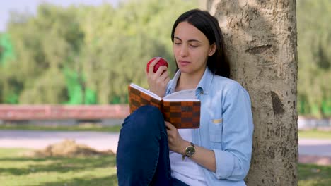 indian girl eating apple while reading the book