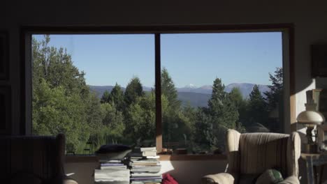 asombrosa vista de la ventana de la gran montaña nevada y la vegetación arbórea desde la acogedora sala de estar con sofás, en una casa elegante a cámara lenta y 60fps