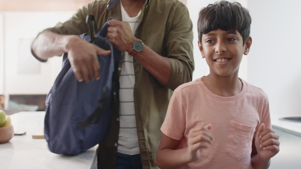 Indian father packing backpack while young son smiling and standing nearby