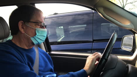 man with face mask wiping and disinfecting steering wheel in the car - handheld, close up