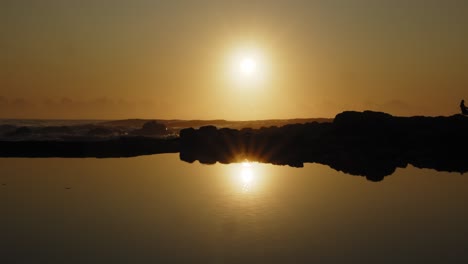 zwolnione ujęcie złotego wschodu słońca nad oceanem odbitego w lustrzanym basenie skalnym