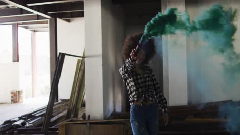 mixed race woman holding green flare dancing in an empty building