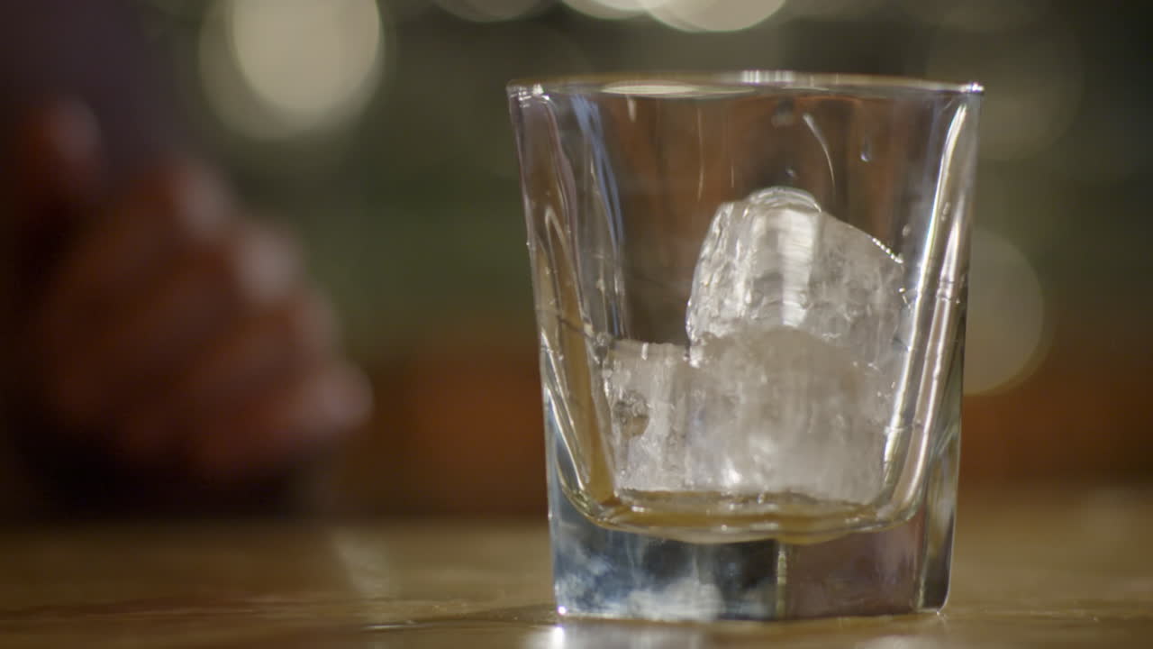 toma en cámara lenta de verter whisky en un vaso con cubitos de hielo