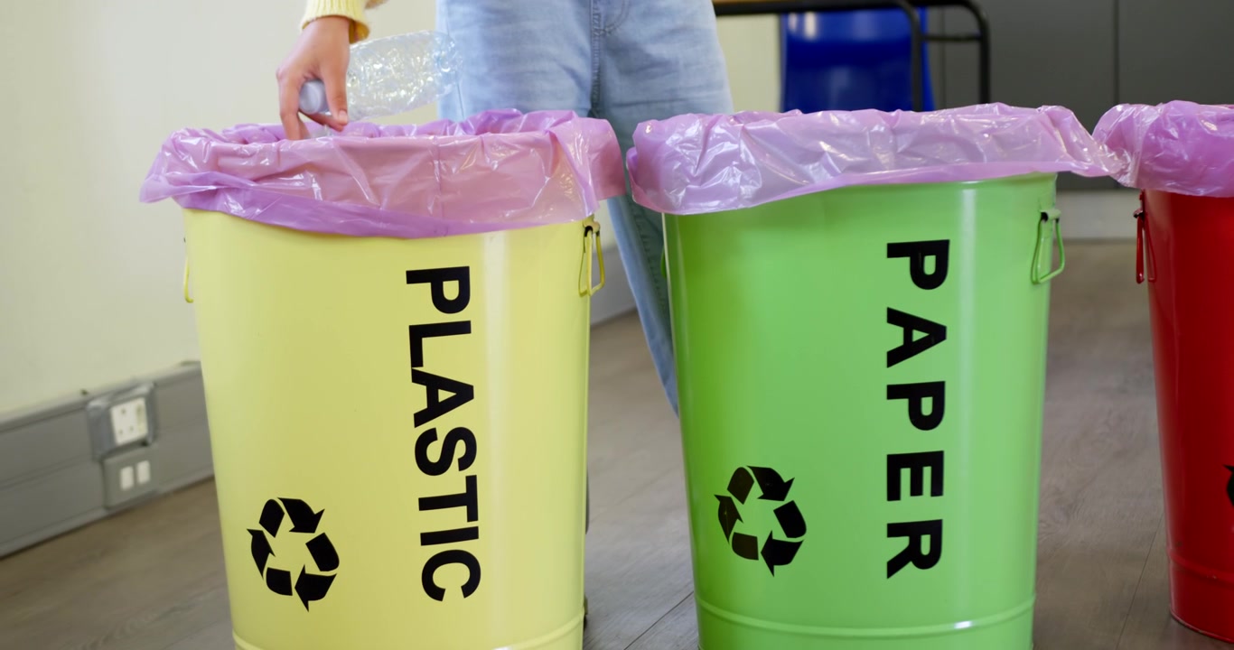 African American youth approaching PLASTIC bin in office, holding clear bottle, dropping to recycle
