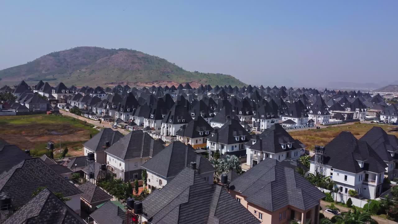 Il drone vola all'indietro sopra un bellissimo quartiere residenziale con case di lusso ad Abuja, Nigeria. Ripresa che si allontana di una serie di case di lusso vicino a una montagna in Africa.