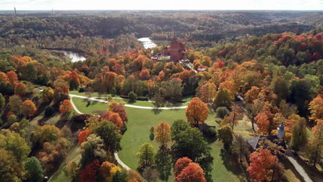 aerial backward moving shot of the turaida castle and river gauja in sigulda, latvia at daytime with the view of pathway going around a beautiful garden