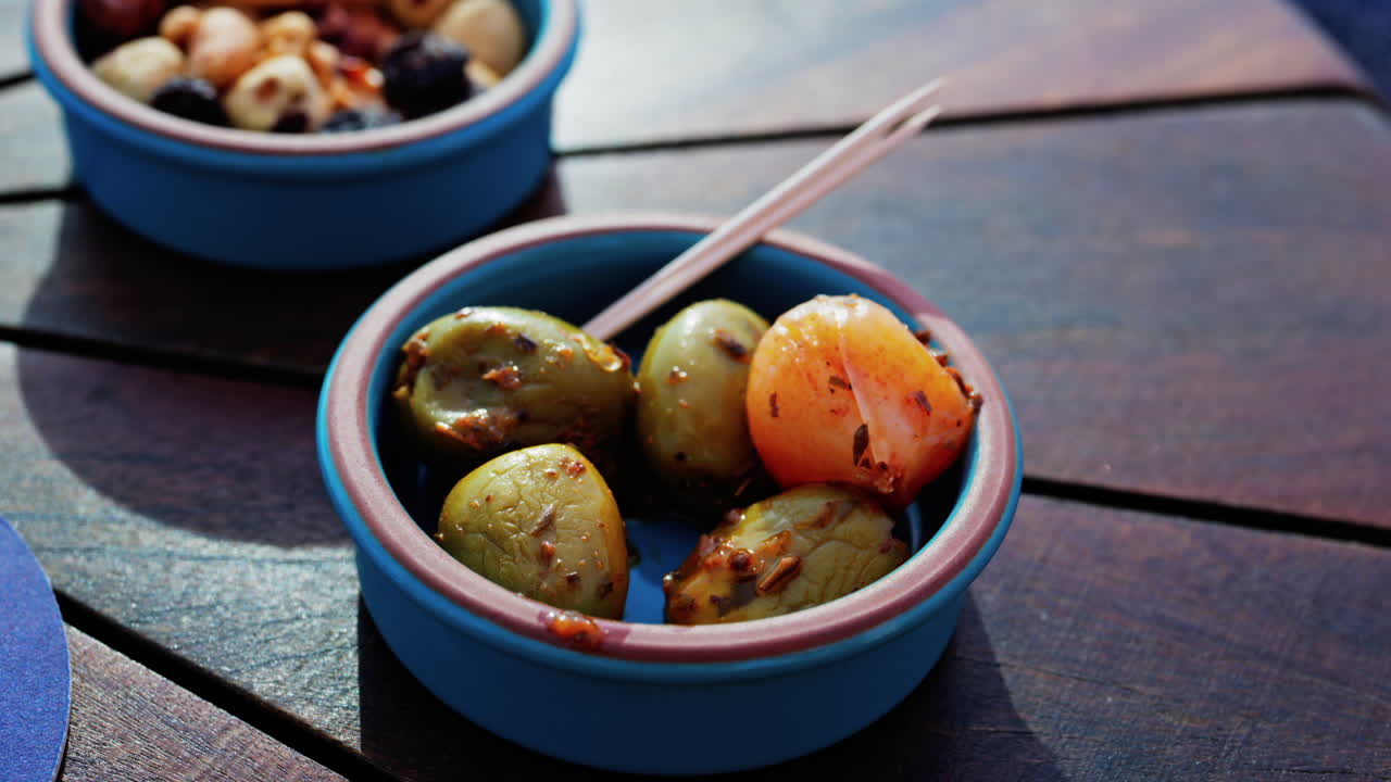 Close up of a hand picking up a green olive with a toothpick on a small bowl on a table