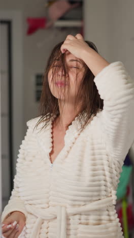 una joven morena escucha música enderezando el cabello mojado después de lavarse en la ducha. una mujer con el cabello húmedo baila mirándose en el espejo en cámara lenta