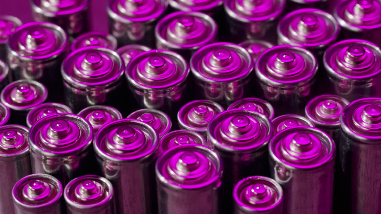 Silver batteries AA and AAA in neon light close-up. Double-A battery is a standard size single cell cylindrical dry battery. Batteries are common in portable electronic devices. An AA battery is composed of a single electrochemical cell that may be either a primary battery or a rechargeable battery.