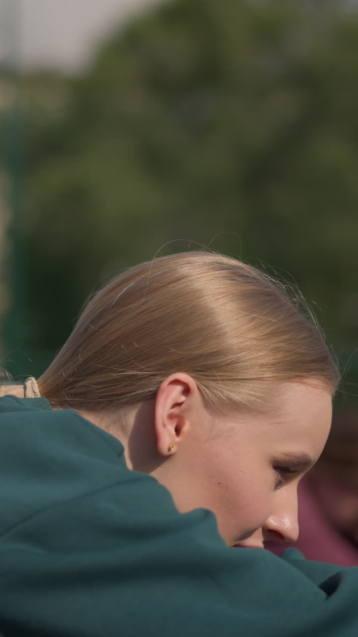 primer plano de una mujer con capucha verde trabajando al aire libre con otras dos damas estirándose en el fondo, mostrando fitness, trabajo en equipo y ejercicio al aire libre en una arena deportiva