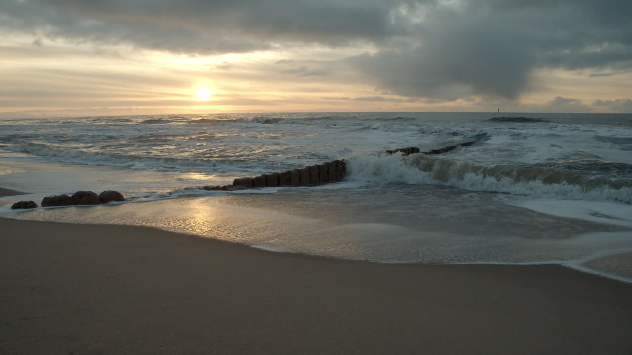 olas rompiendo en los espigones de la isla sylt con la puesta de sol en el fondo