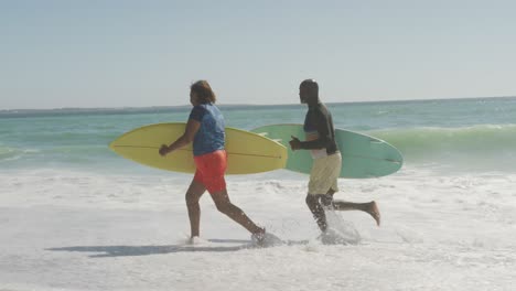 senior african american couple running with surfboard on sunny beach