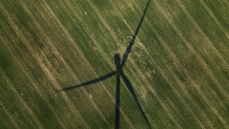 a movie shot from a drone, the shadow of a windmill in the field, the camera is rotating