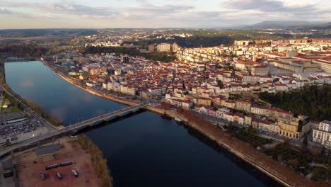Aerial-view-of-coimbra-Portugal-city-of-famous-university,-drone-fly-above-the-river-and-bridge-during-golden-hour