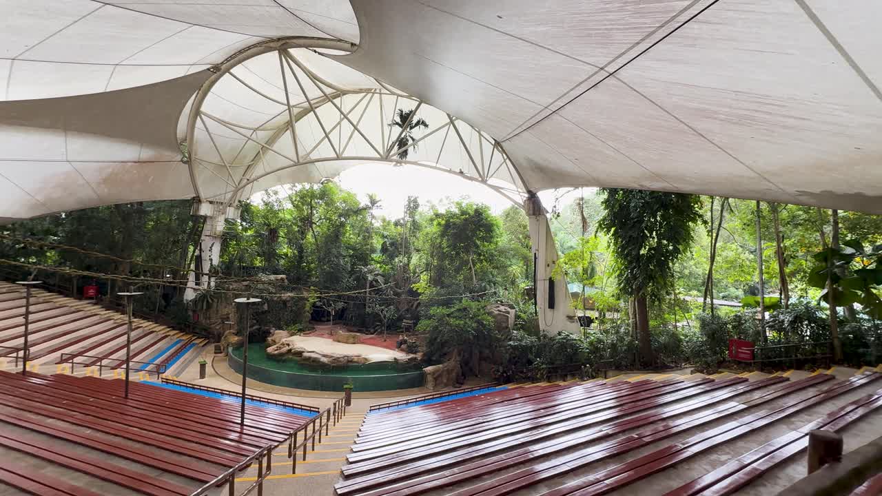 Wide angle panning shot of an empty outdoor animal show arena with lush jungle foliage