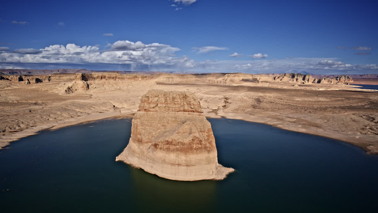 Drone gliding above Lake Powell, showcasing a towering rock formation amidst the vast desert canyon scenery.