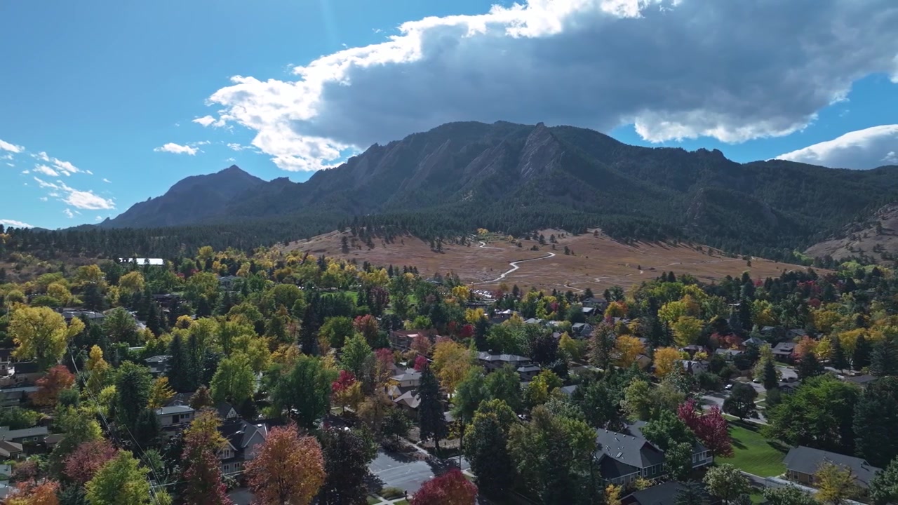 Case suburbane di Boulder e il vivace centro città circondati da un vibrante fogliame autunnale e dalle Flatirons retroilluminate, ripresa aerea con tracciamento a sinistra