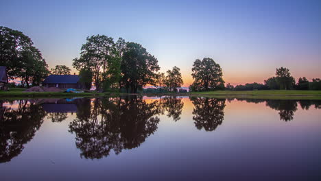 Timelapse-of-sunrise-behing-remote-lakeside-cabin-reflecting-in-water