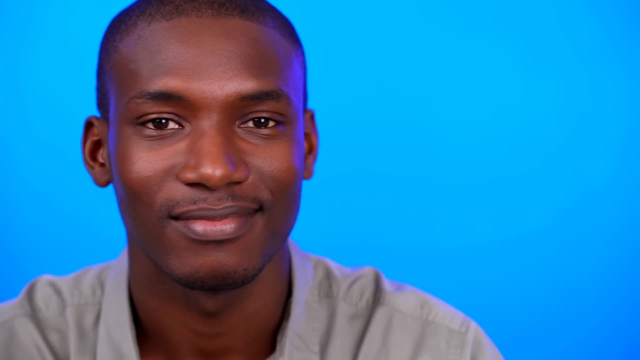 Black Man Portrait On Blue Background, Studio Headshot With Subtle Smile, Shifting Gaze, Casual Shirt, Soft