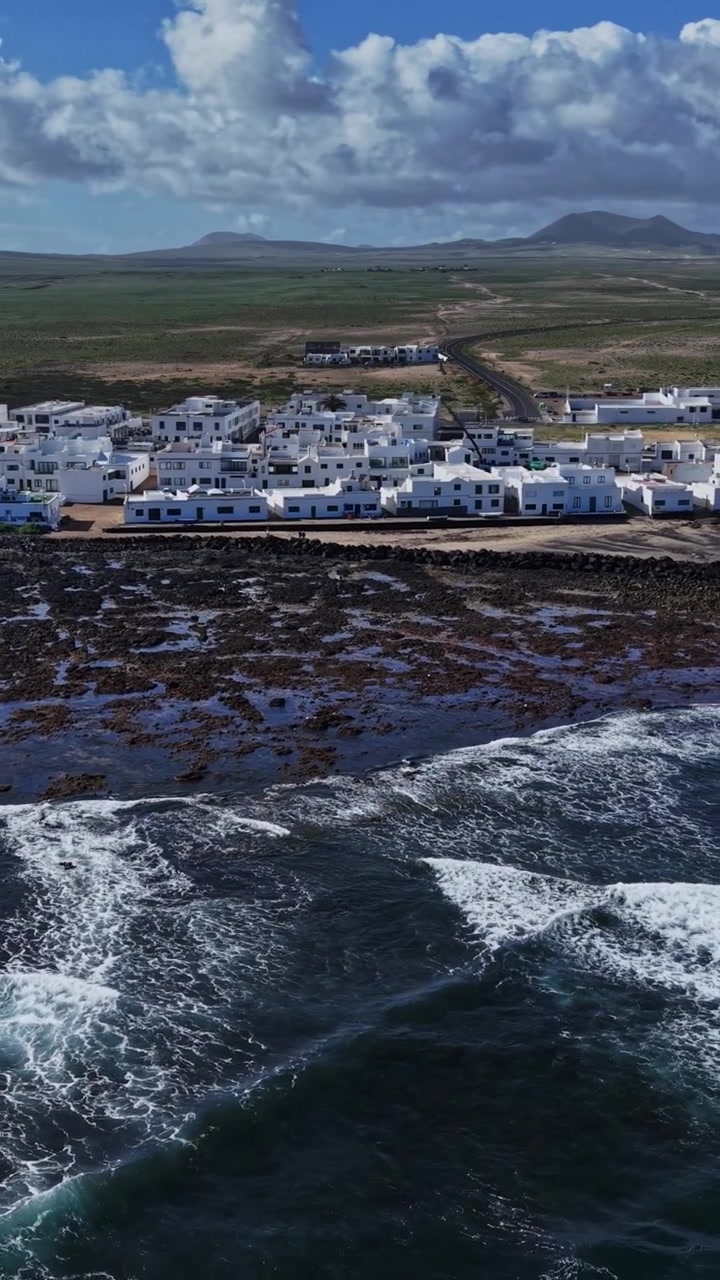 Vista costiera di Lanzarote con edifici e onde in primo piano.