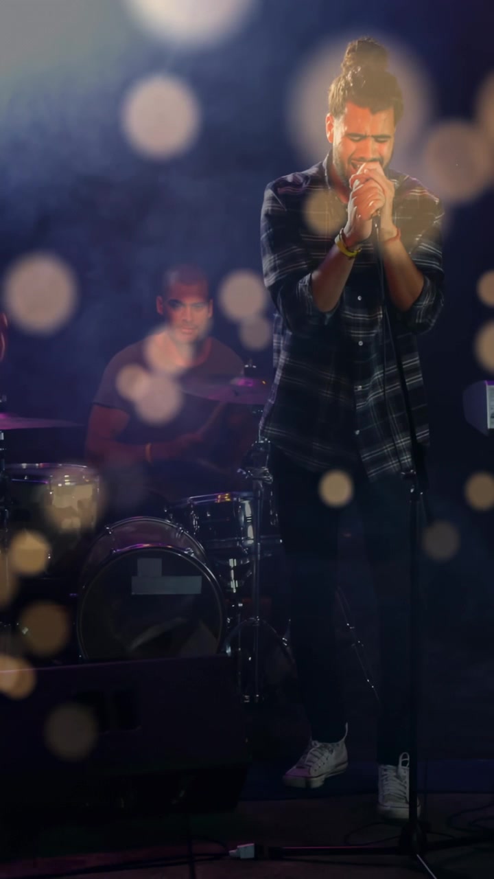 Video verticale: Cantante solista dopo la battuta del batterista, che canta nel microfono per la musica, con effetto bokeh sul cantante.