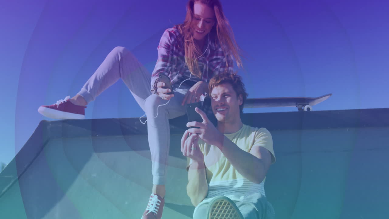 male and female friends sharing smartphone content at skatepark, displaying animated tech icons