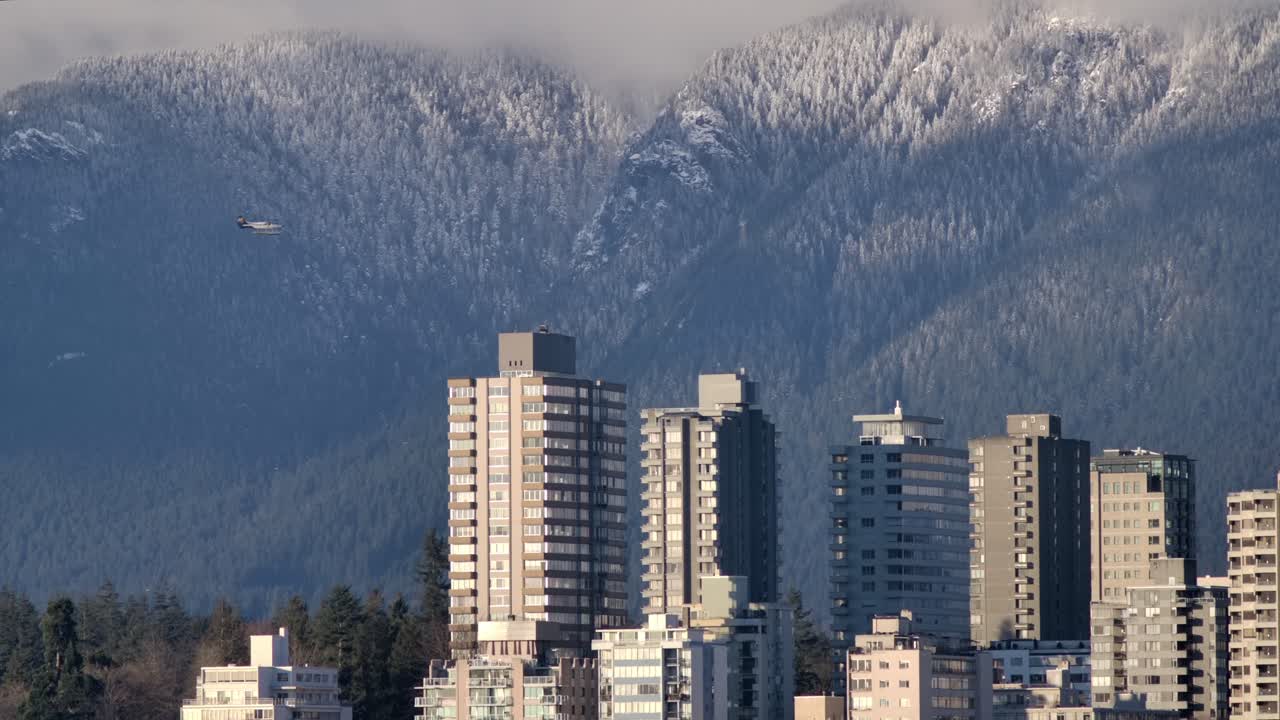 Flugzeug fliegt über Küstenstadtlandschaft und winterliche Waldberge in Vancouver, British Columbia, Kanada.