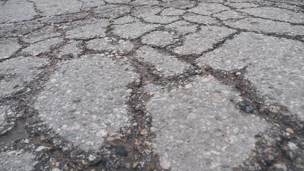 Vista dettagliata di una superficie stradale in asfalto danneggiata e crepata.